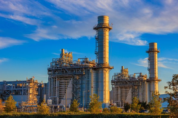 Natural gas-fired turbine power plant with its cooling towers rising into a cloud-filled blue sky.