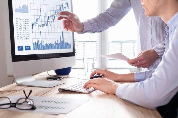 Two professionals researching stock charts on a monitor.