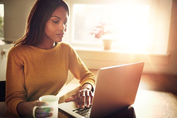 A woman using a laptop and holding a coffee mug.