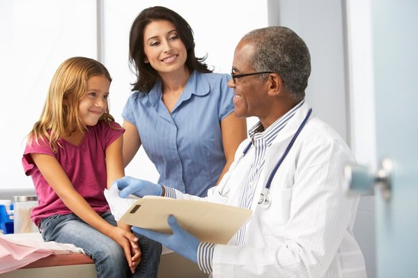 A woman and girl talk with a doctor in a hospital room.